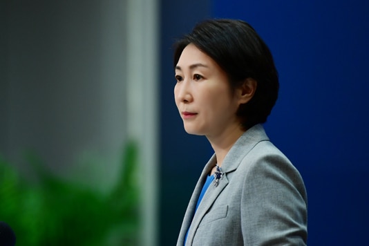 A Chinese woman with short hair standing in grey blazer at podium looking off camera.