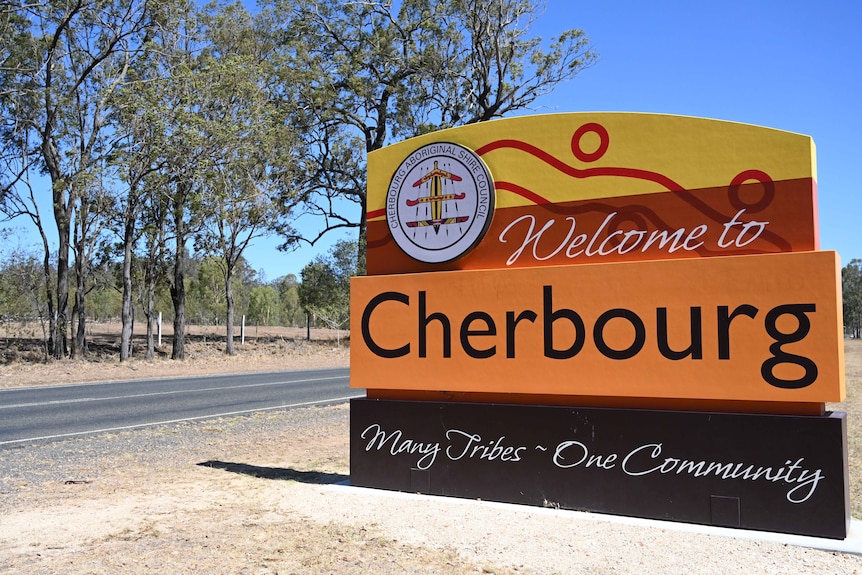 A bright orange and yellow welcome sign stands as a greeting to motorists driving into Cherbourg.
