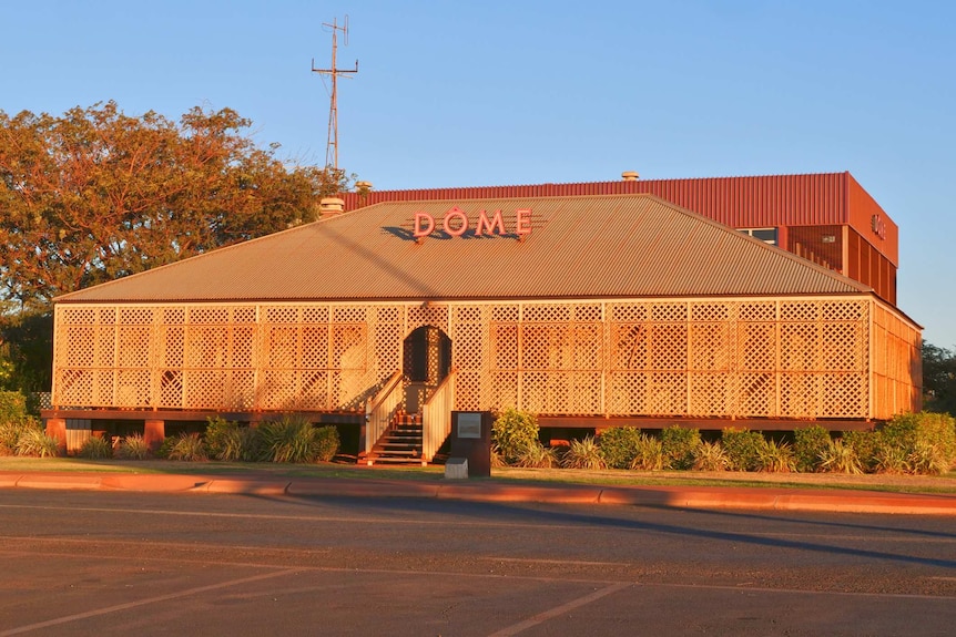 An old homestead with lattice work around it covered in red dust.