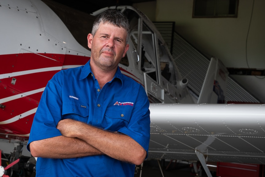Crop dusting pilot standing in front of small plane with his arms crossed