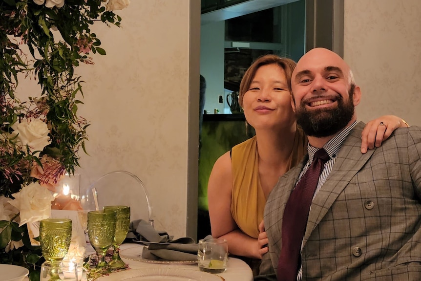 A woman and a man pose over a candelit dining table