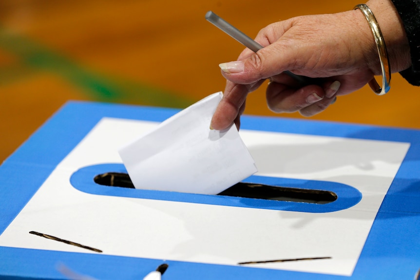 a woman putting a voting ballot paper in a box