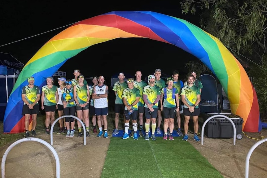 A group of runners stand underneath an inflatable rainbow.
