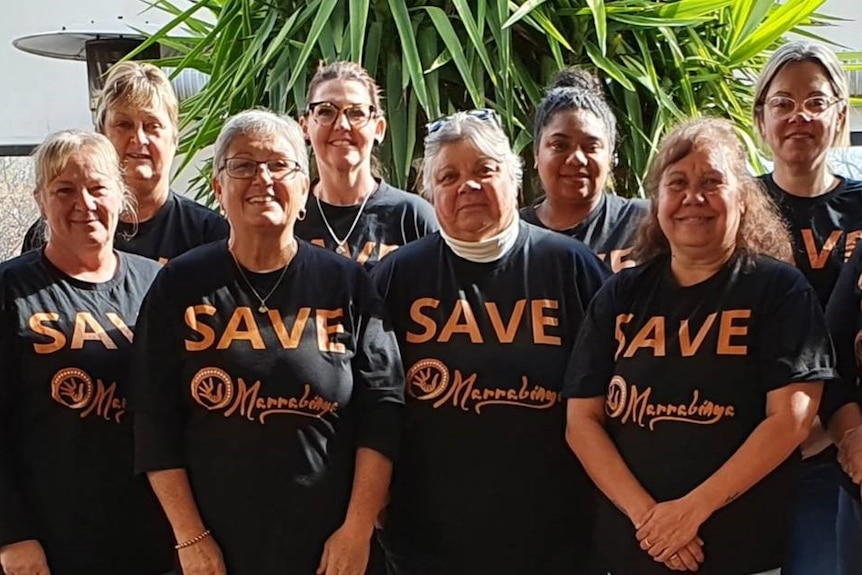 Ten women standing in a line in front of a plant wearing black tshirts with 'save marrabinya' on them.