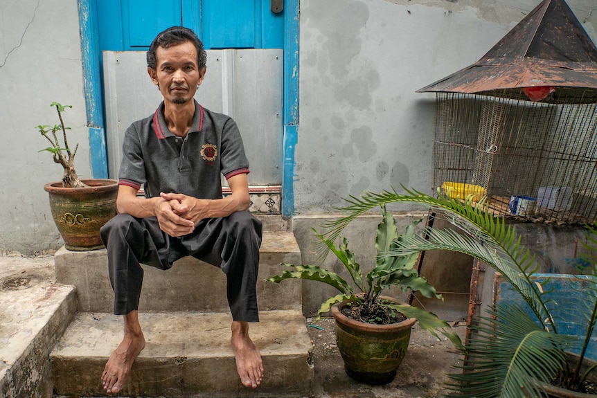 An Indonesian man sits on a stoop, surrounded by plants