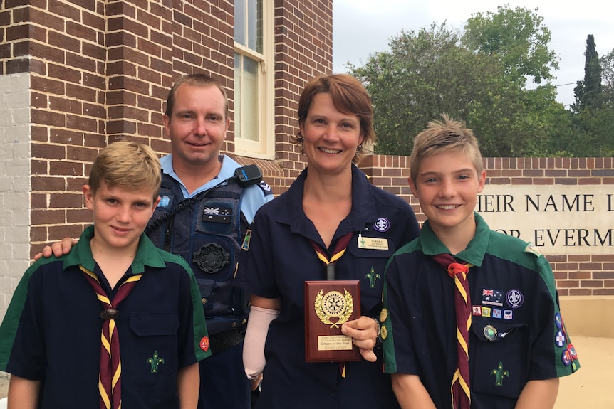 A woman with an amputated arm holds an award with a man and two boys beside her.