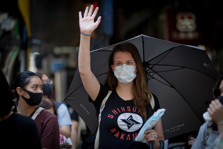 Woman puts one hand up as she holds an umbrella.