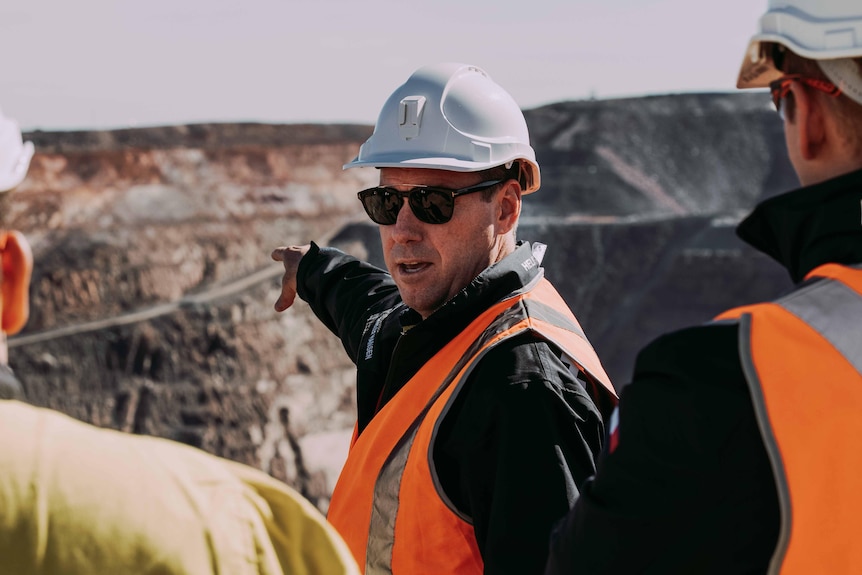 A man wearing a high-vis vest and hard hat on a mine site