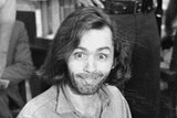 Charles Manson sits in a courtroom chair, leering at the photographer and sticking his tongue out