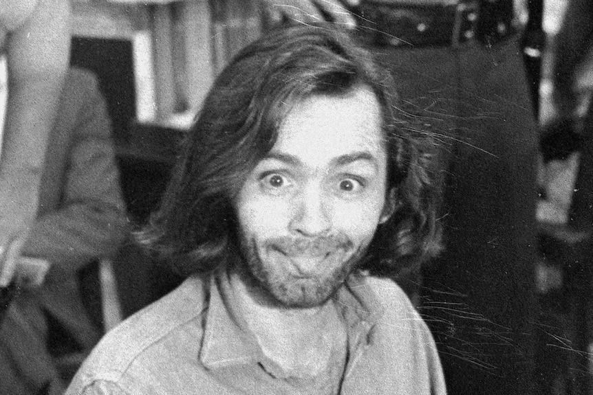 Charles Manson sits in a courtroom chair, leering at the photographer and sticking his tongue out
