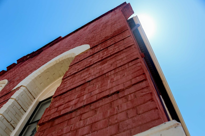 The exterior of a red brick building with blue sky and bright sun visible.