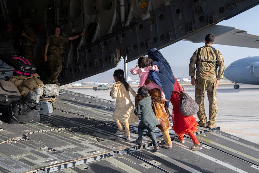 A woman with five small children walk into the back of an aircraft at Kabul airport.