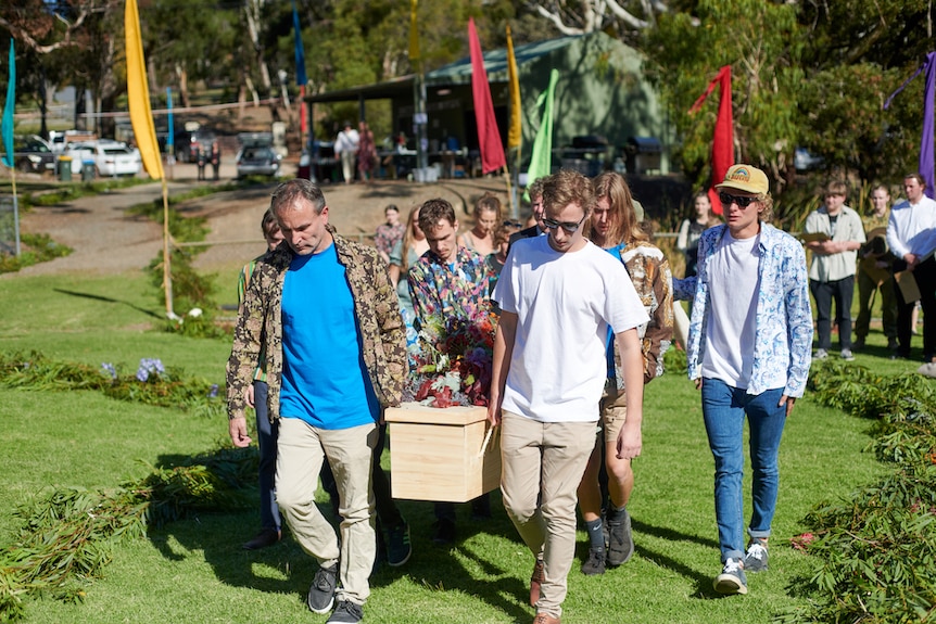 A group of men carrying a coffin at an outdoor park. 