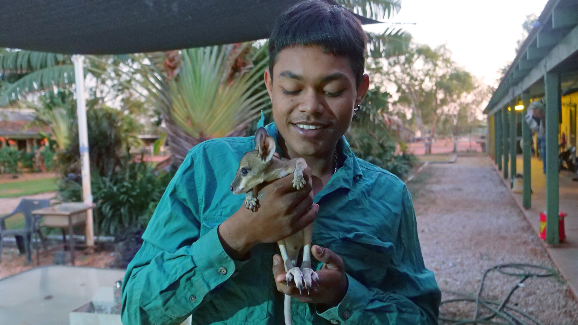 A young man holds a joey in his arms. He is smiling.