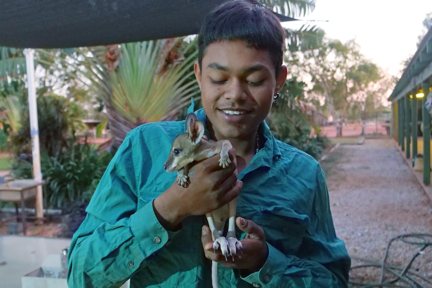A young man holds a joey in his arms. He is smiling.