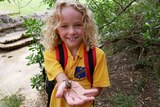 A school girl holds a small crab in the palm of her hand.