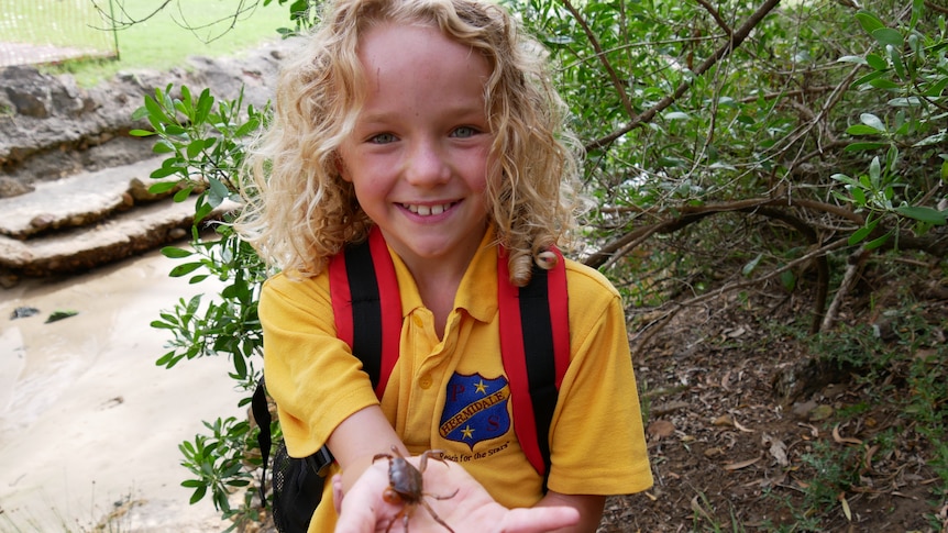 A school girl holds a small crab in the palm of her hand.