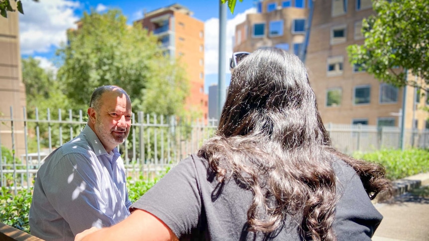 Nark Morey in a business shirt on the left speaks with a woman whose face is turned away from camera.