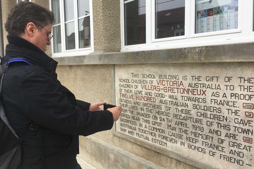 A man wearing a black jacket taking a photo of a sign at Villers-Bretonneux in France.