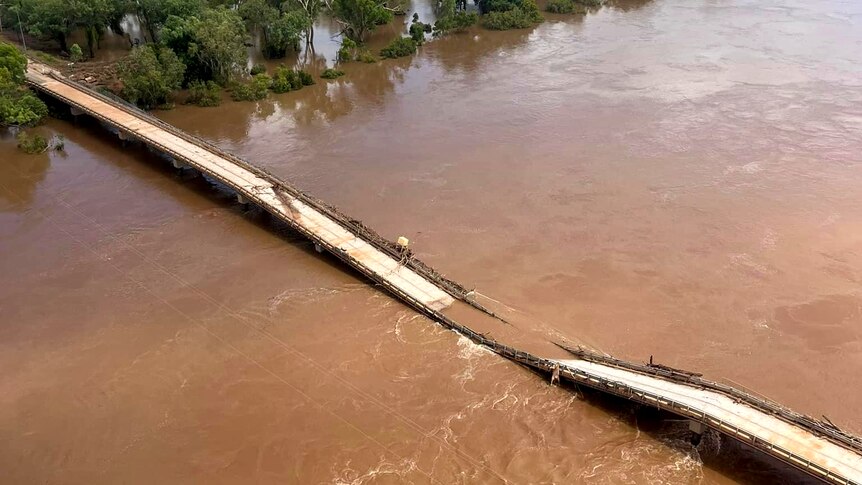 A destroyed bridge lays in a bloated brown river
