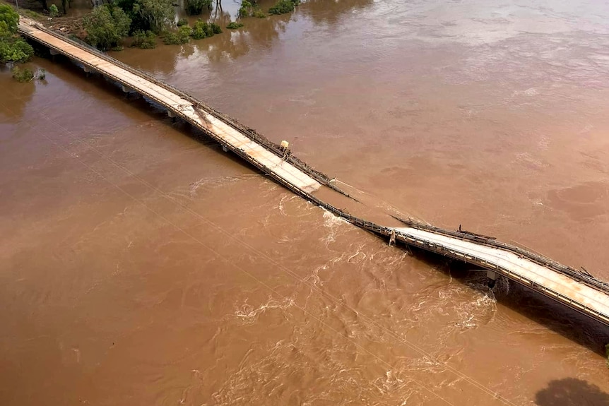 A destroyed bridge lays in a bloated brown river