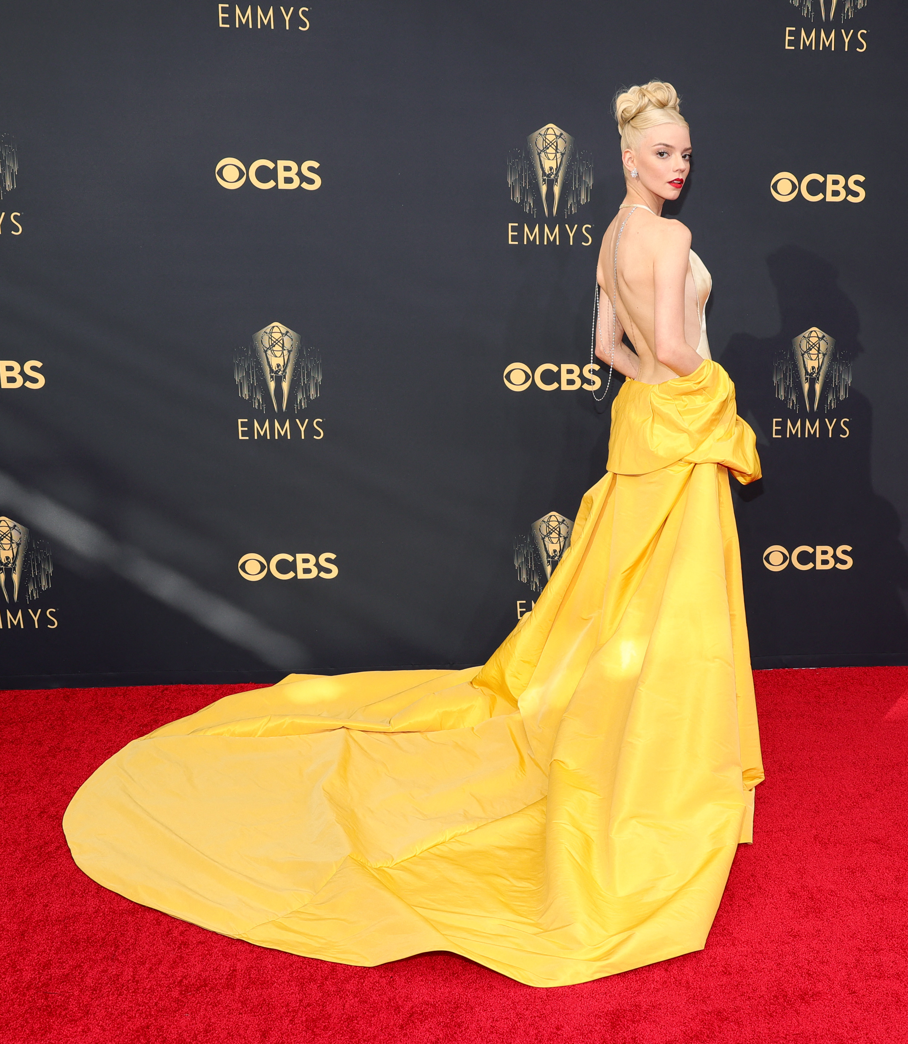 Anya Taylor-Joy in a backless white dress with a long yellow cape worn off the shoulder.