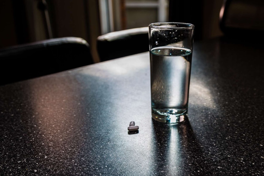 A glass of water and Panadeine tablet on a table.
