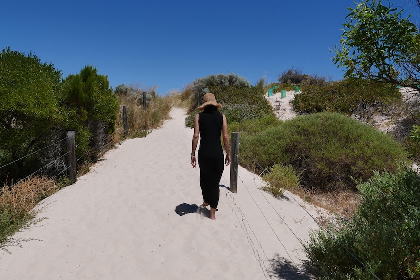A woman walks up a sand dune, pictured from behind.