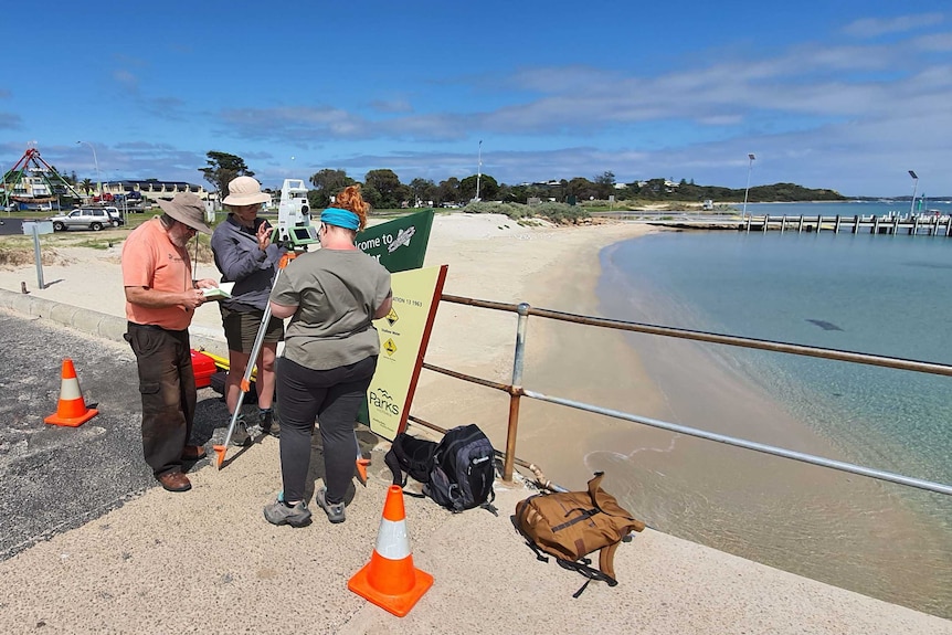 Three people standing on a wharf looking at mearusing instruments