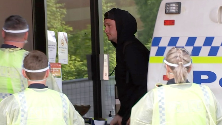 A man carries a bag and leaves the back of a police car.