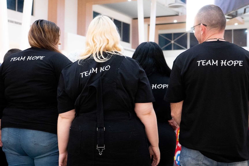 a group of people with their backs to the camera wearing black shirts which say 'team hope'