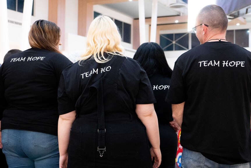 a group of people with their backs to the camera wearing black shirts which say 'team hope'