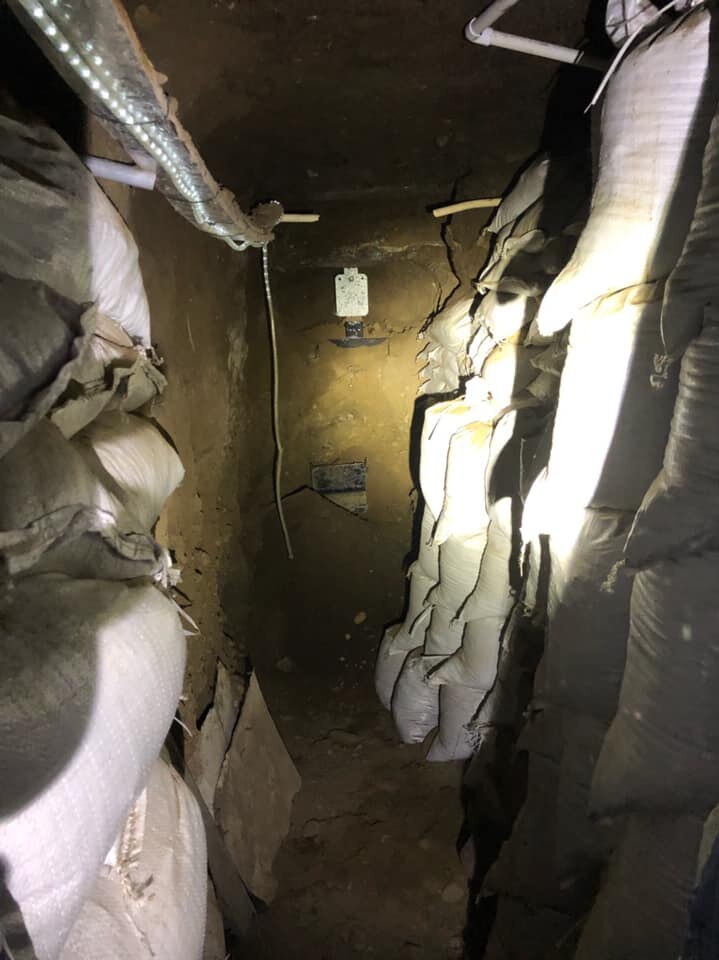 A narrow passage dug into earth is lined with sandbags and lit with electric lights.