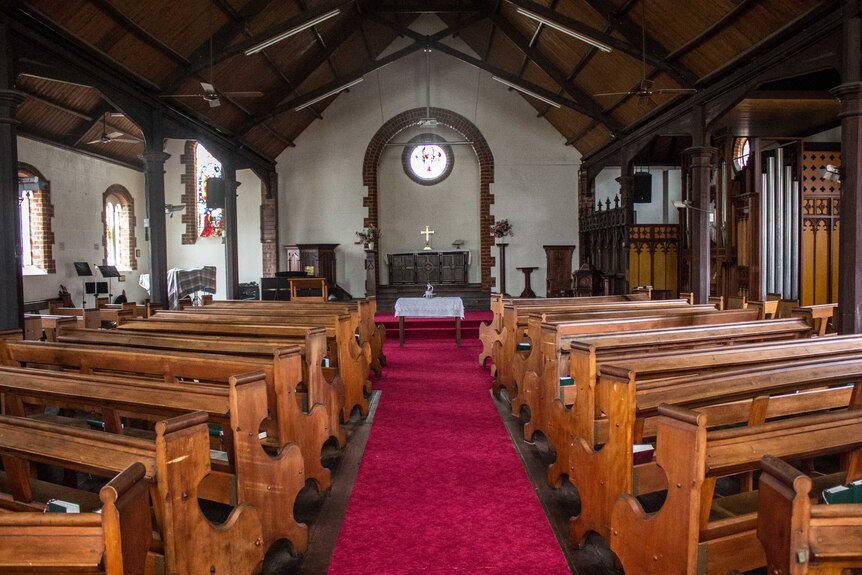 The empty interior of St Alban's Church in Highgate with wooden benches and a red carpeted aisle.