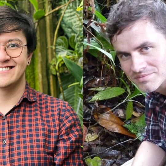 Two people surrounded by lush foliage. One with dark short hair and glasses, other with dark short hair. Checked shirts