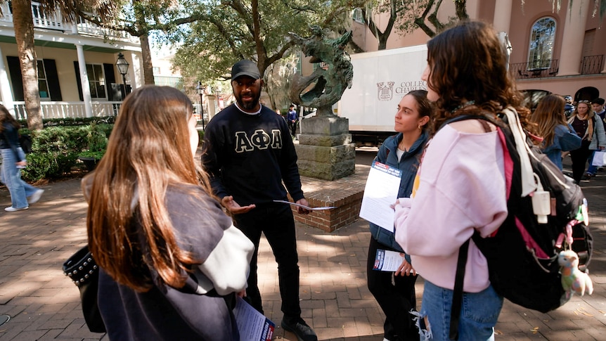 African American man speaking to three college students about voting.