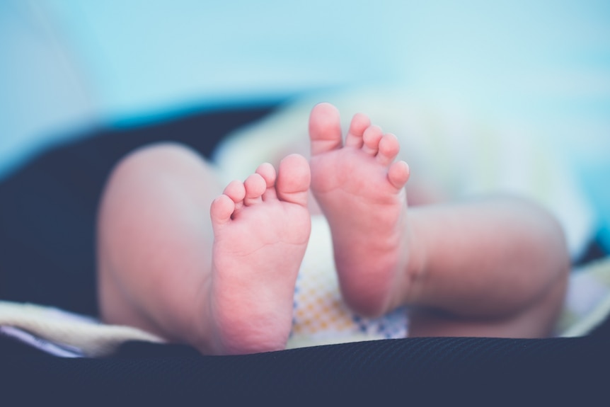 The feet of a newborn baby are in focus with its nappy and body out of focus.