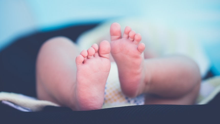 The feet of a newborn baby are in focus with its nappy and body out of focus.