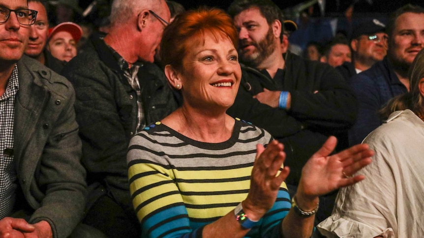 Pauline Hanson smiles and claps her hands in a crowd of men.
