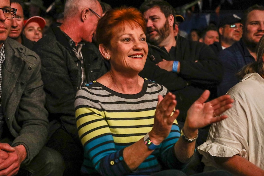 Pauline Hanson smiles and claps her hands in a crowd of men.