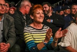 Pauline Hanson smiles and claps her hands in a crowd of men.