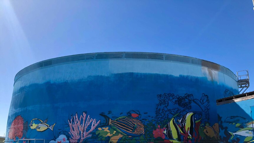 A large water towen in Bowen being painted into a mural of the ocean.