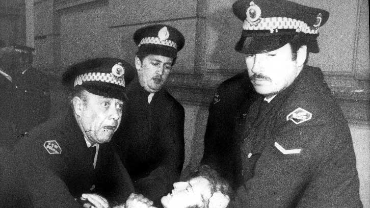 Four policemen hold on to a protester, one of whom is grabbing his hair.