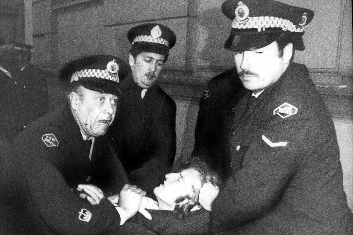 Four policemen hold on to a protester, one of whom is grabbing his hair.