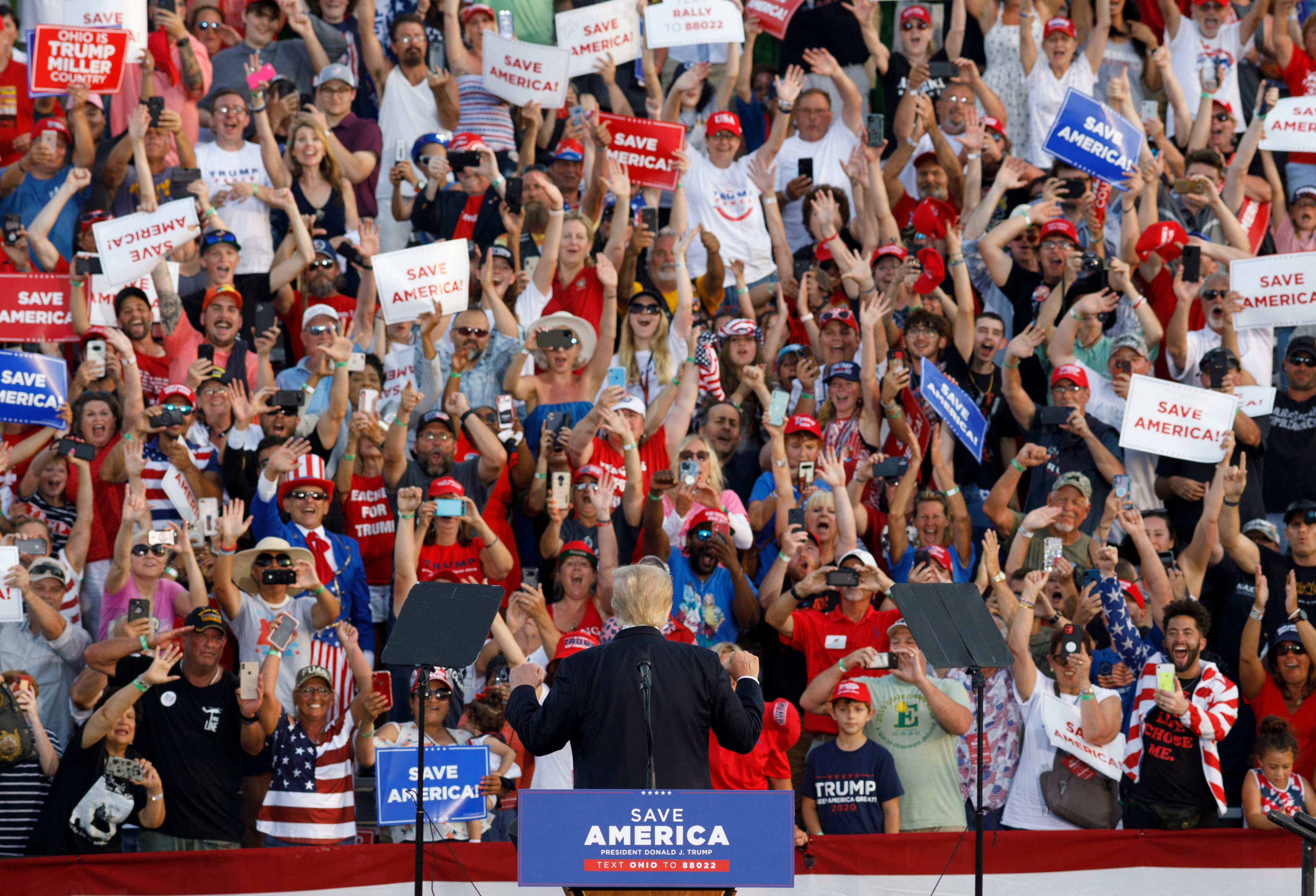 Donald Trump turns from his lectern to face a sea of cheering supporters on stadium seating behind him.