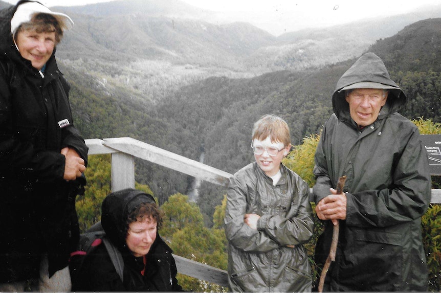 A family, including a young boy, pose for a photo with a mountainous landscape in the background.