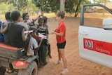 Erin interviewing Aboriginal children sitting on all-wheel drive vehicle with ABC Kimberley car door in shot.