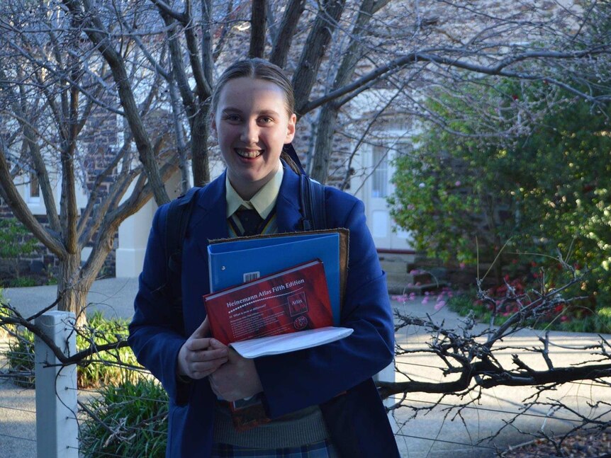 A teenage girl in a school uniform and blue blazer holding school books