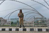 Security guard holds a gun and stands in front of wire fence