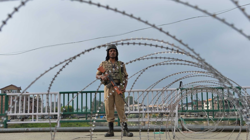 Security guard holds a gun and stands in front of wire fence